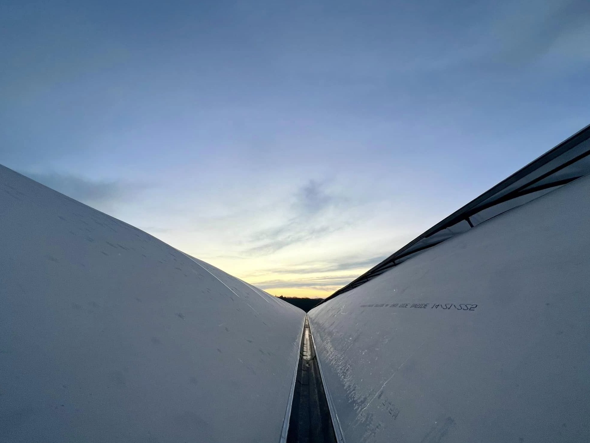 Two arched greenhouse roofs meeting against a sunset sky