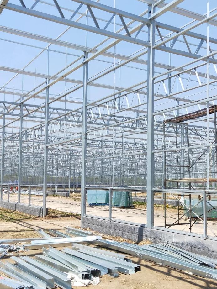 Galvanized greenhouse frame with stacked rigid panels ready for glazing