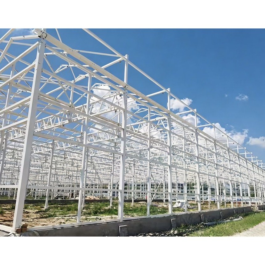 White painted steel frame of a glass greenhouse under a blue sky