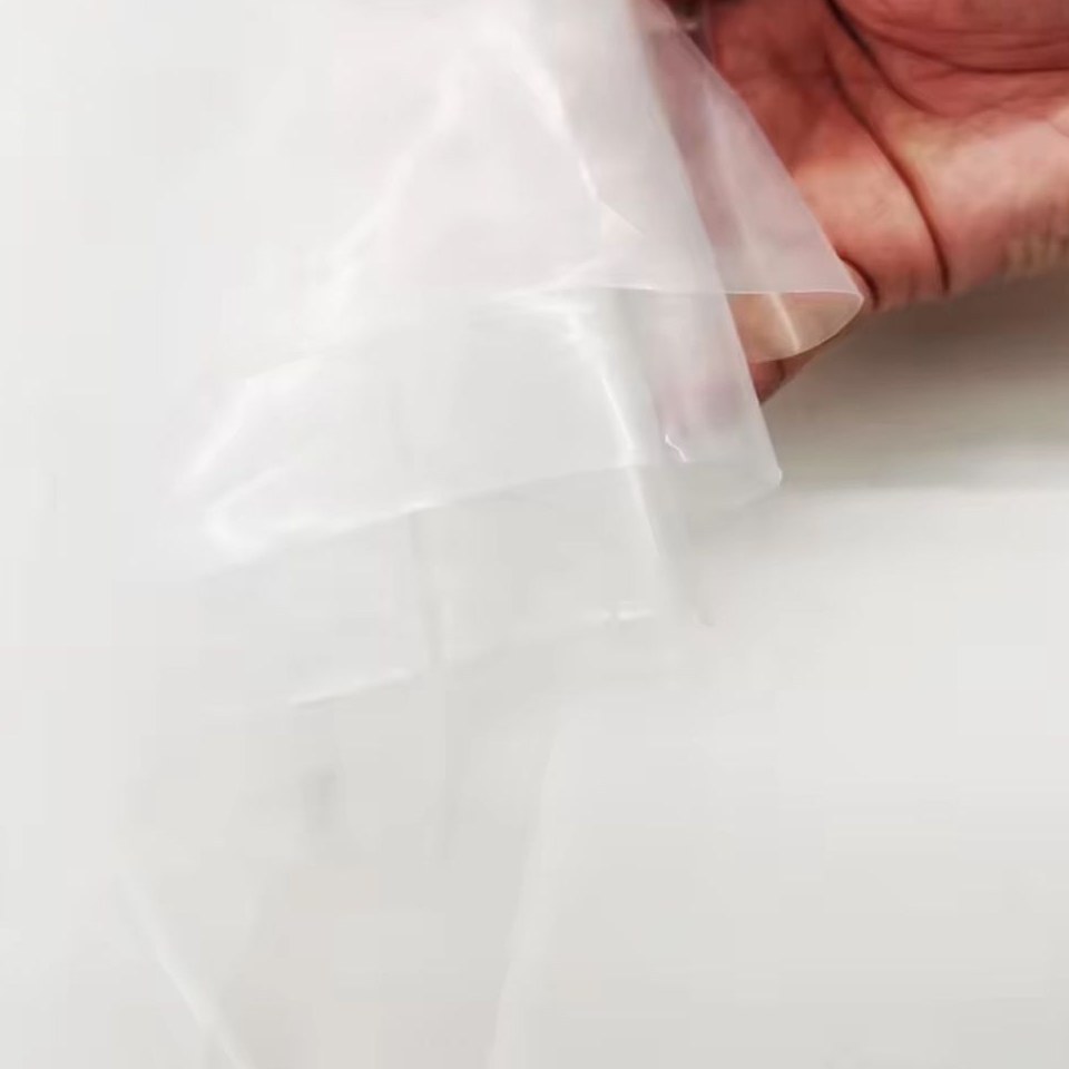 Hand holding a sample of clear greenhouse film to show transparency