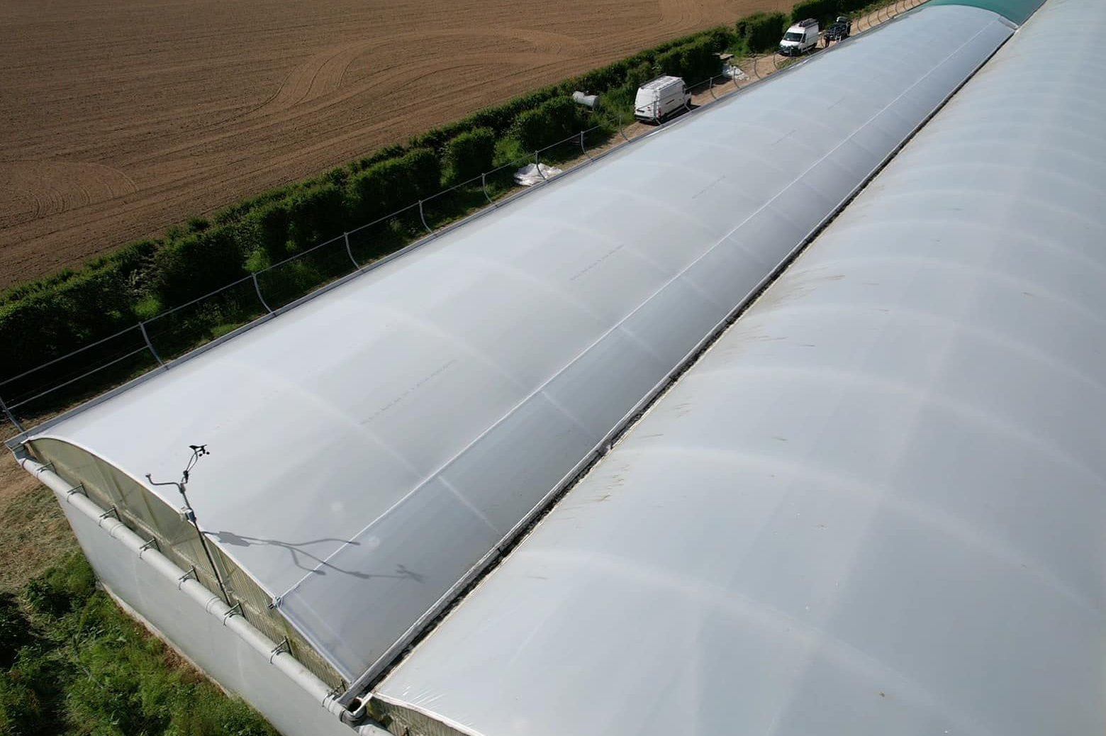 Side view of multi span film greenhouse roofs along a field boundary