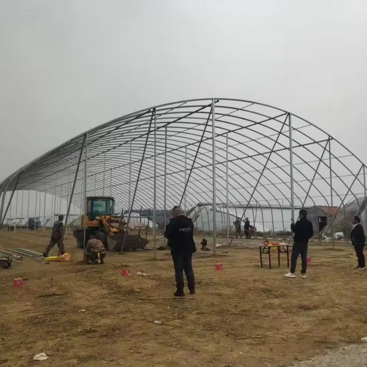 Installation team and machine working on site beside a new greenhouse frame
