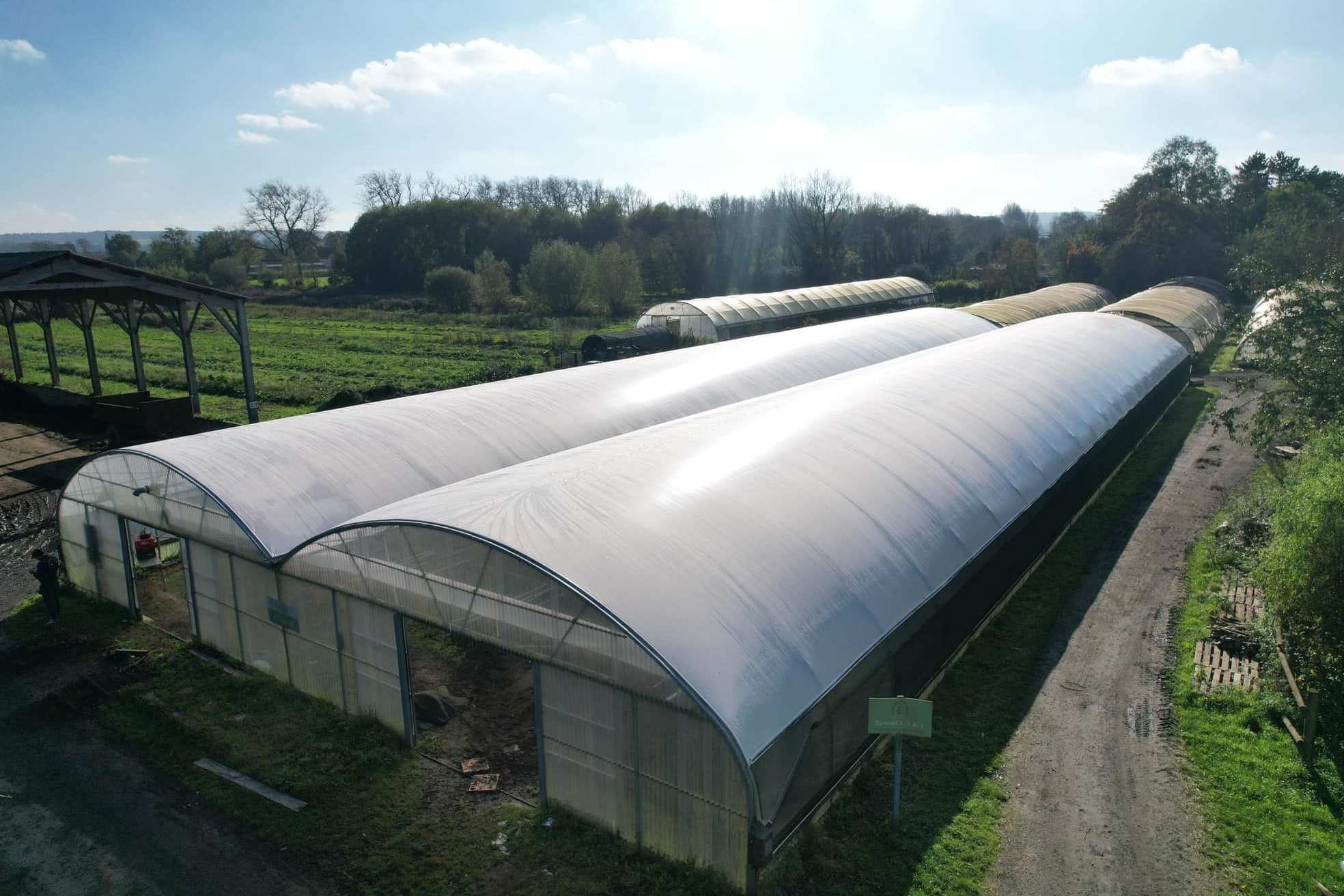 Row of film tunnel greenhouses on a farm under a blue sky