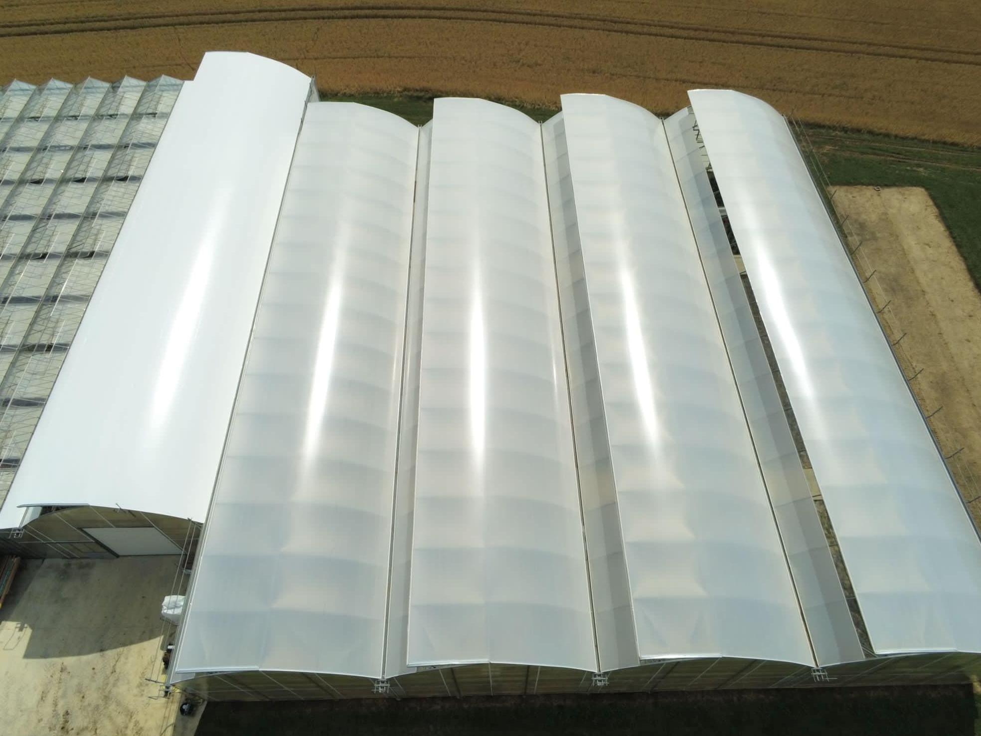 Overhead view of linked arched tunnel greenhouse roofs beside a field