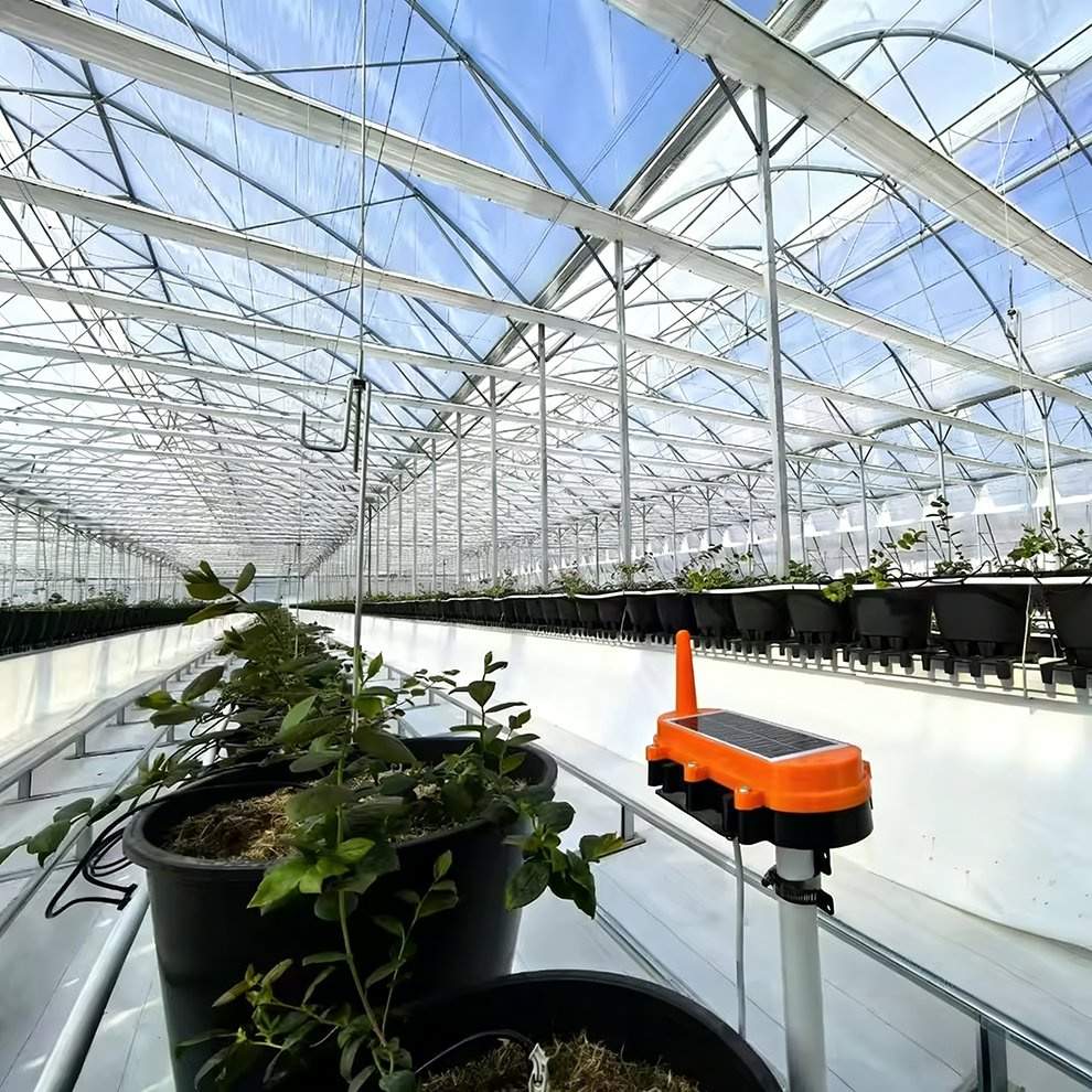 Solar powered device mounted on a bench post among potted plants inside the greenhouse