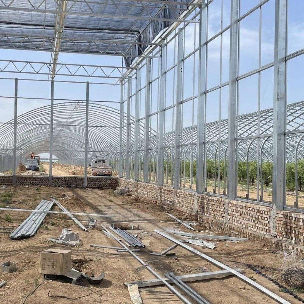 Glass greenhouse frame and glazing under construction on a prepared site