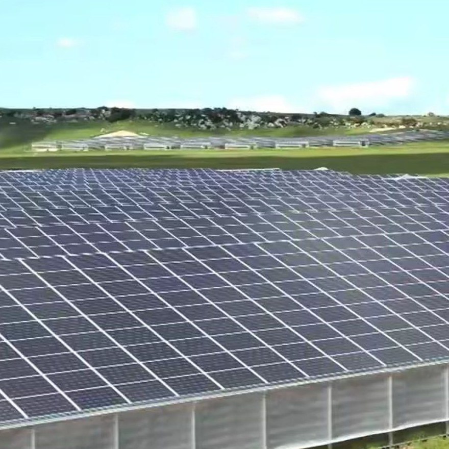 Multi span glass greenhouses with roof mounted solar arrays in a field