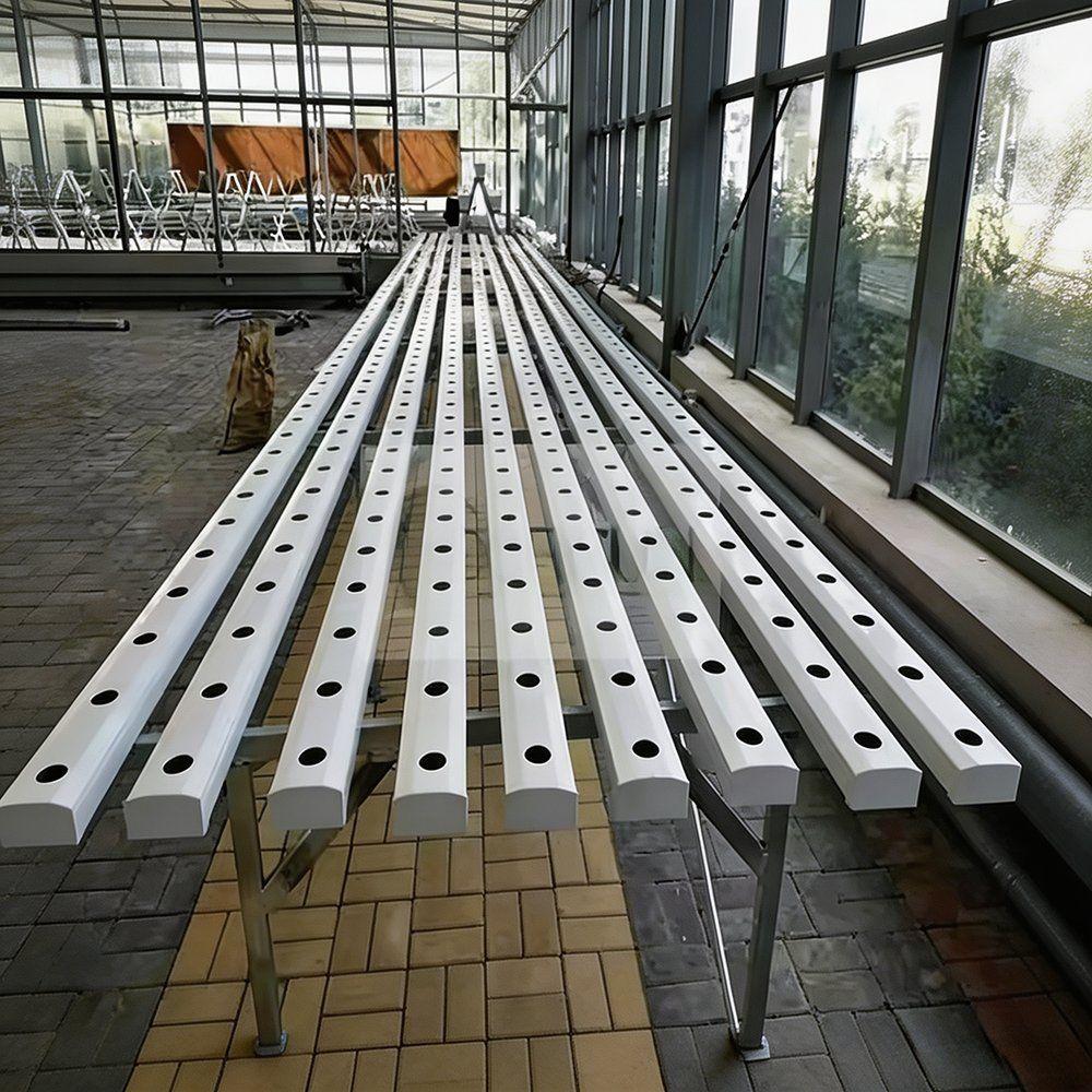 Empty white hydroponic channel rows laid out inside a greenhouse