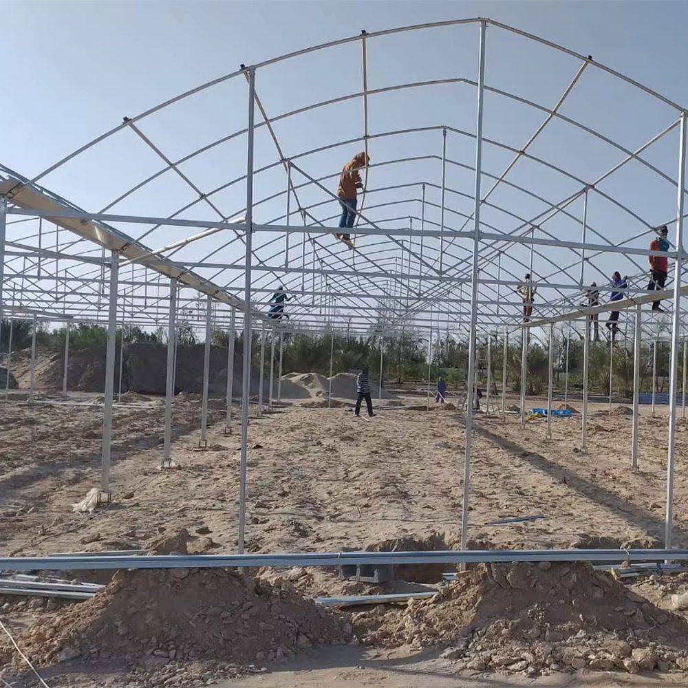Steel greenhouse frame under construction with workers on the structure
