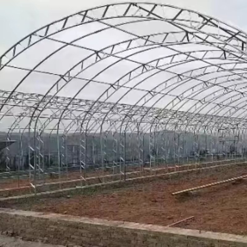 Arched steel greenhouse frame standing on a prepared site