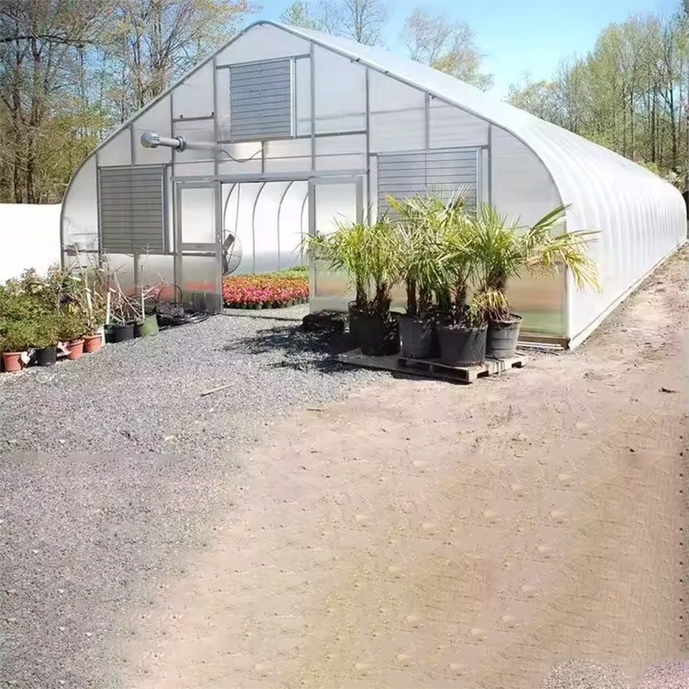 Tunnel greenhouse with potted plants standing in front of the entrance