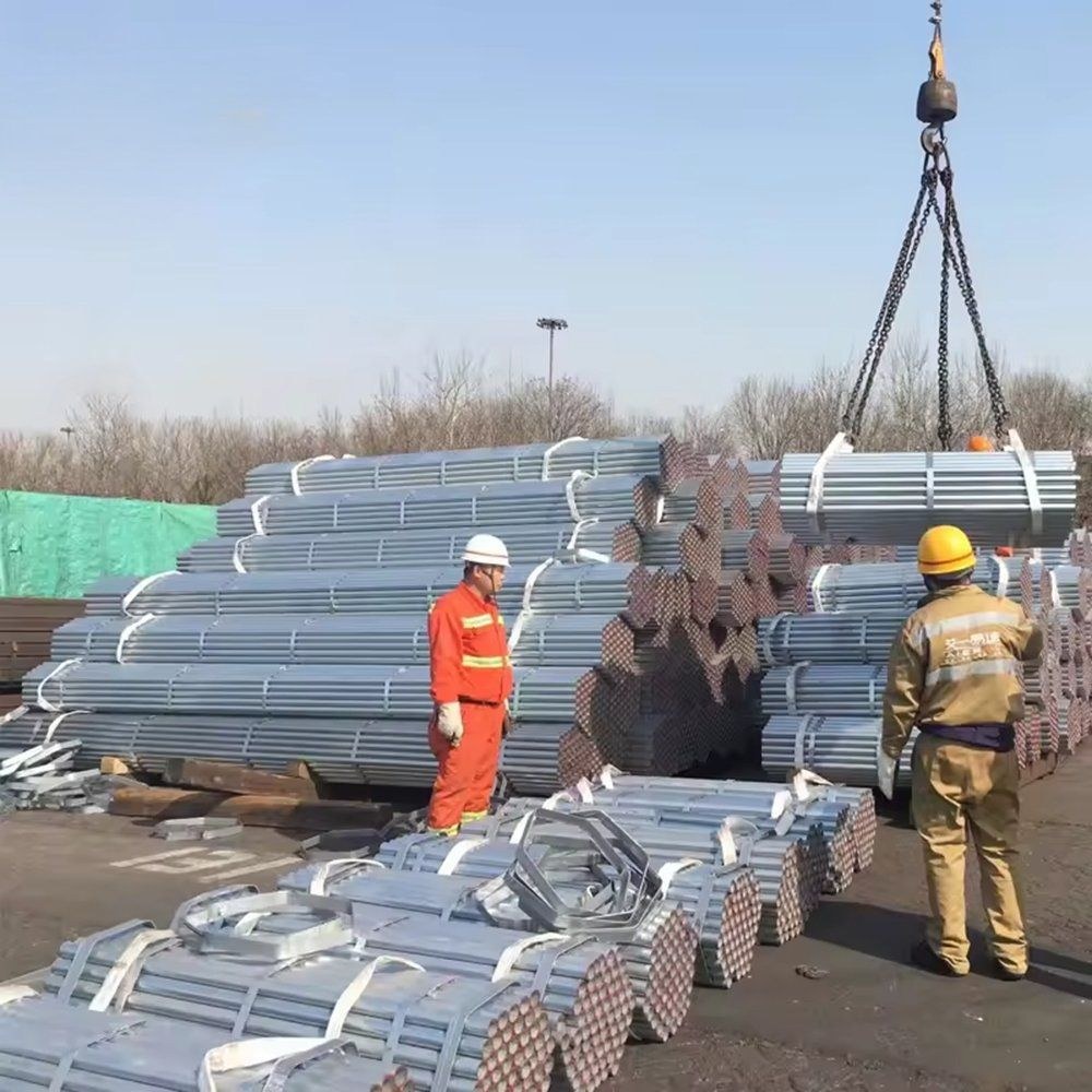 Workers loading bundles of galvanized steel pipe with a crane