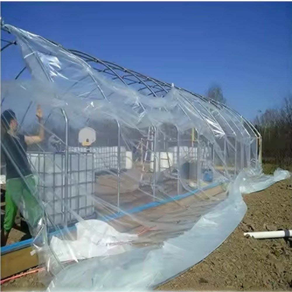 Film being pulled over the frame of a gothic arch greenhouse
