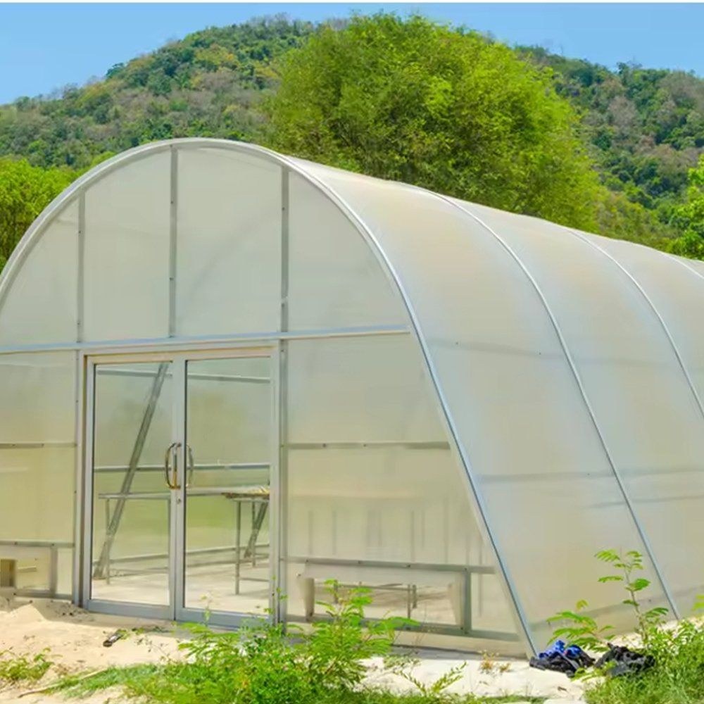 Arched film greenhouse standing in front of trees on a hillside site