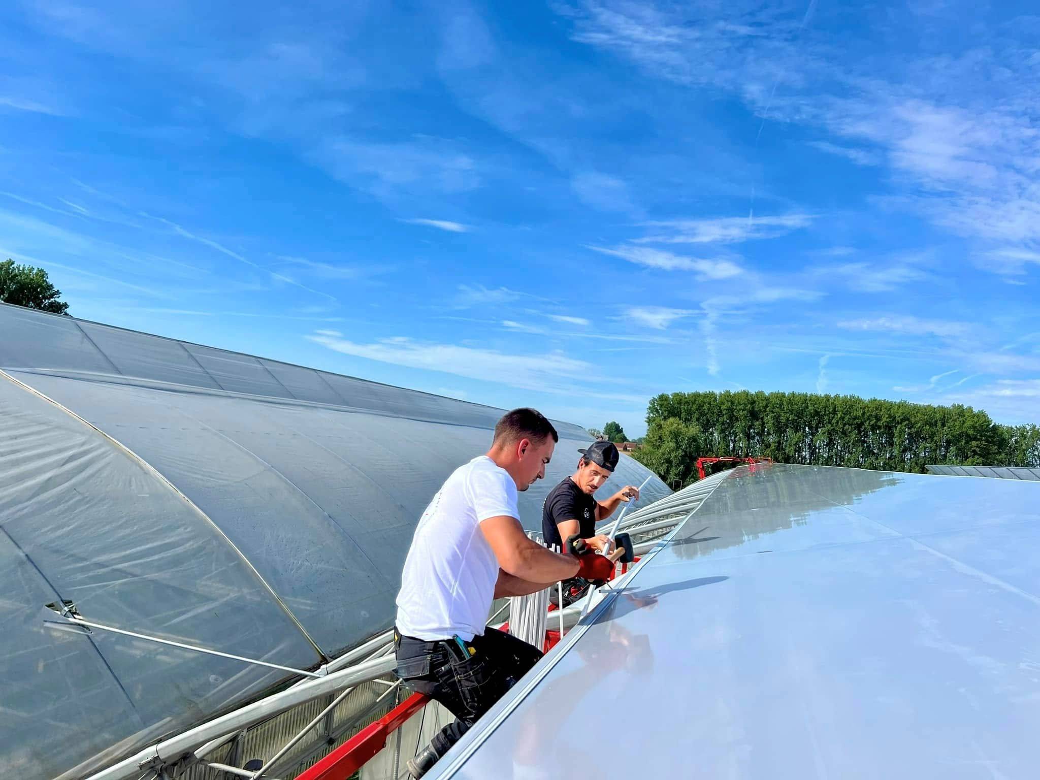 Workers fixing glass roof panels onto a greenhouse frame