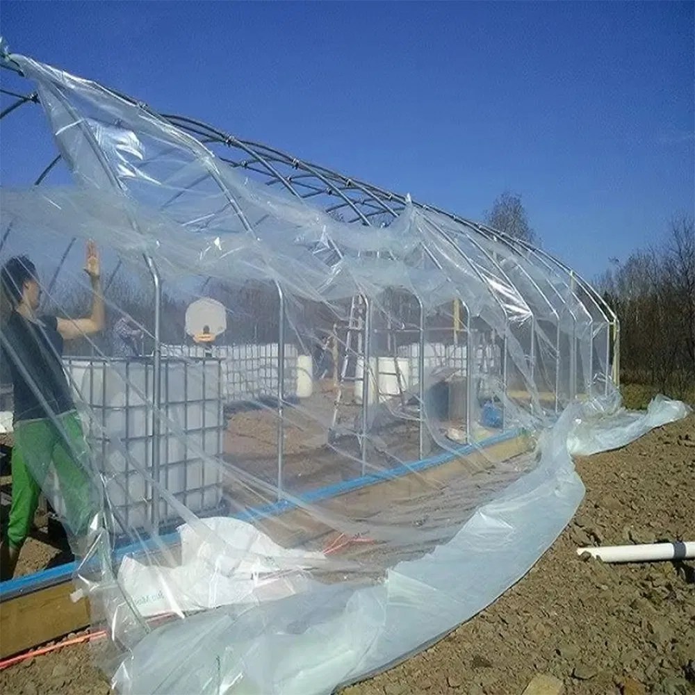 Workers pulling polyethylene film over a steel tunnel frame during construction