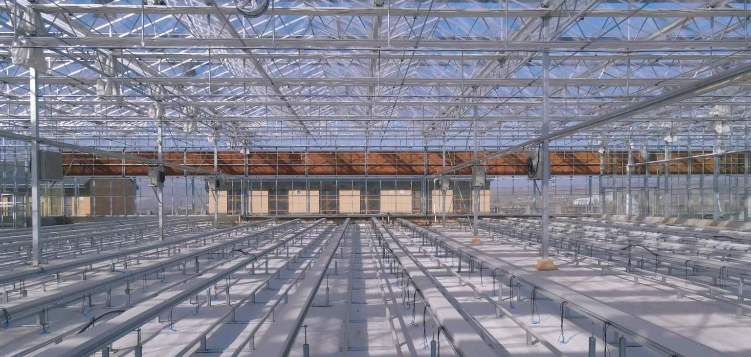 Interior of a large glass greenhouse with benches and rails installed