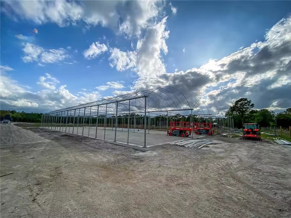 Construction machinery working beside greenhouse frames on site